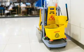 A janitorial cart with mop bucket and wet floor sign in a public building