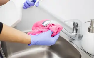 Gloved hands cleaning a stainless sink and chrome faucet