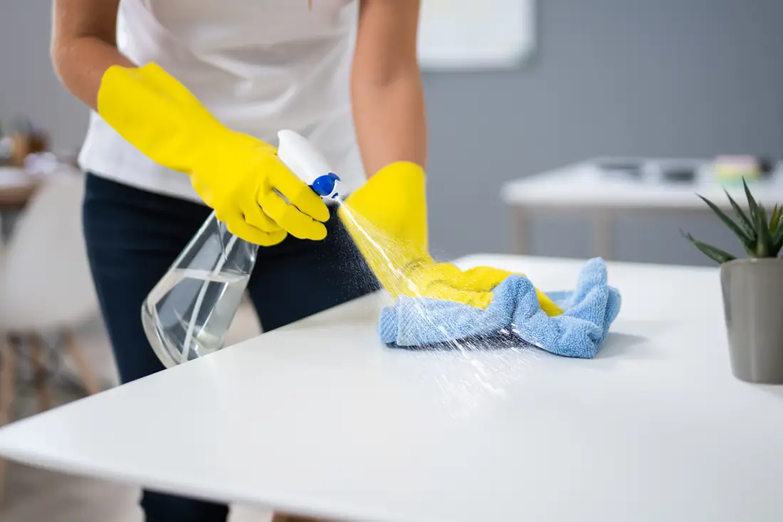 A cleaner wiping down a desk surface